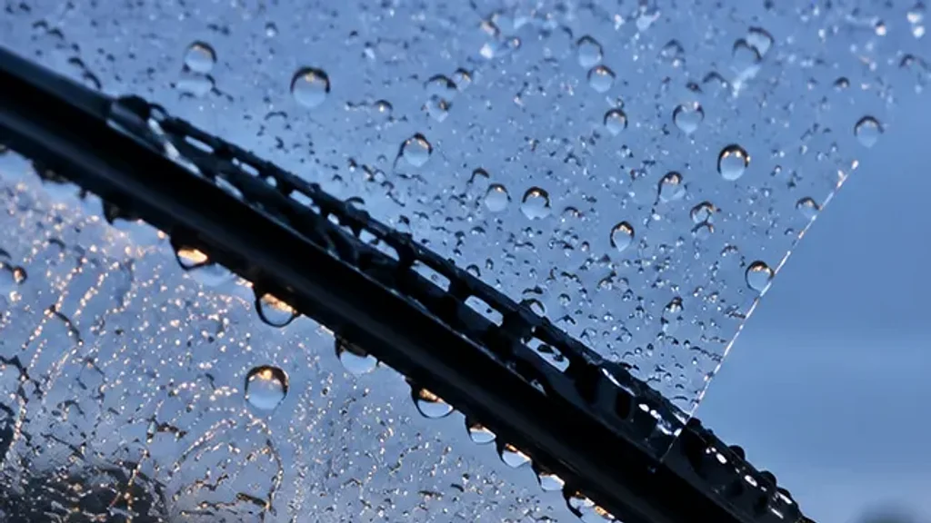 A wiper blade on a rain-covered windscreen at dusk