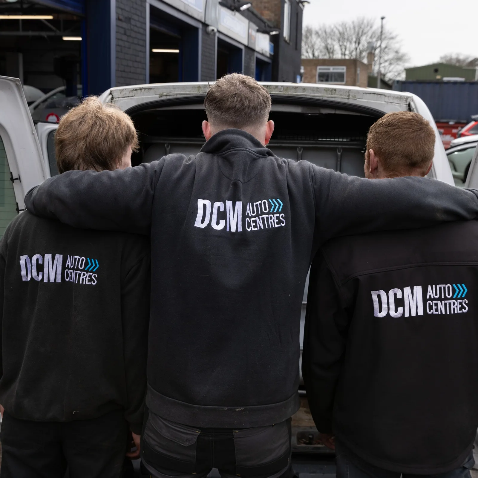 Three DCM Autocentres technicians in branded jackets