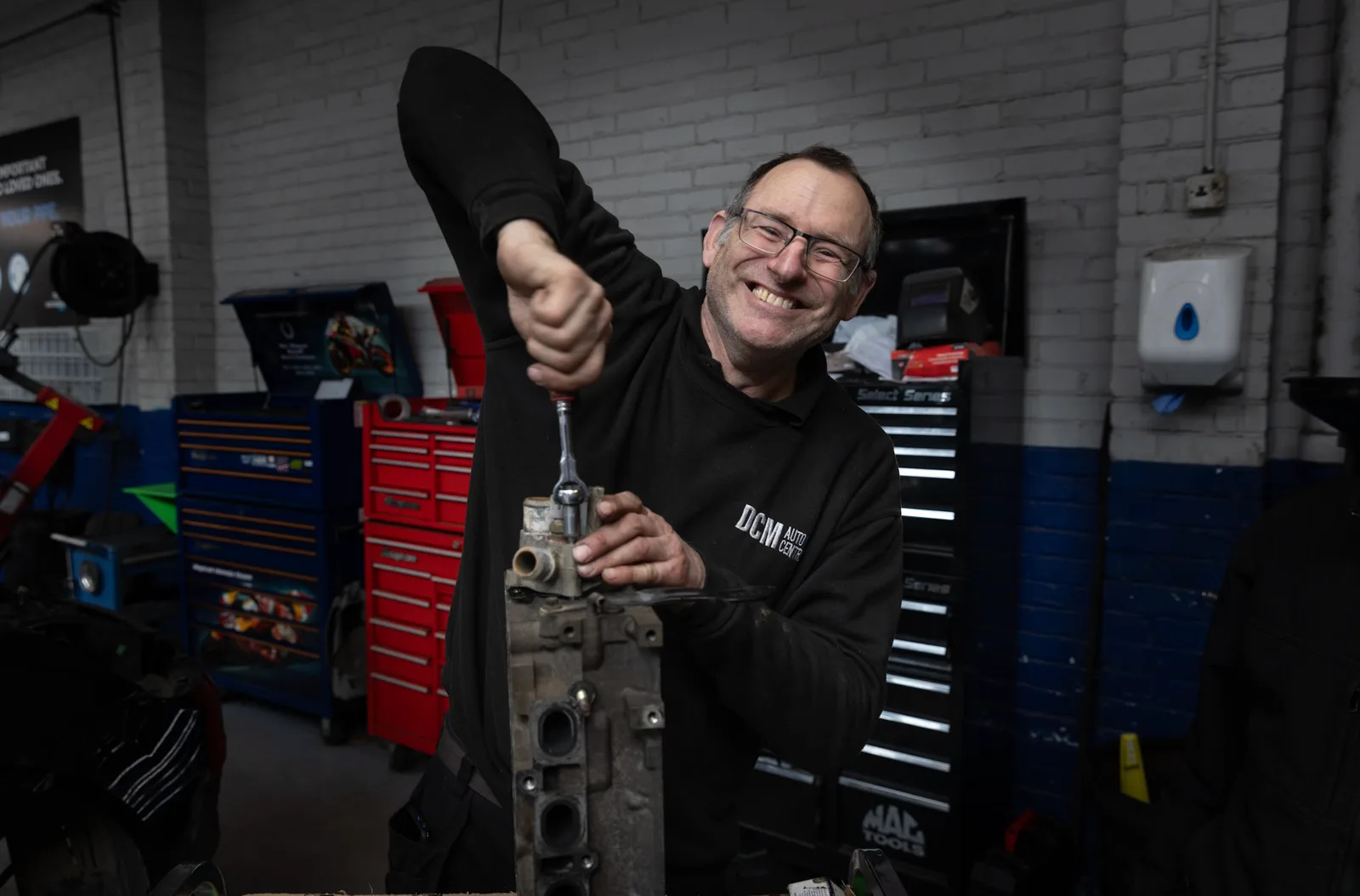 A smiling DCM Autocentres technician working on an engine