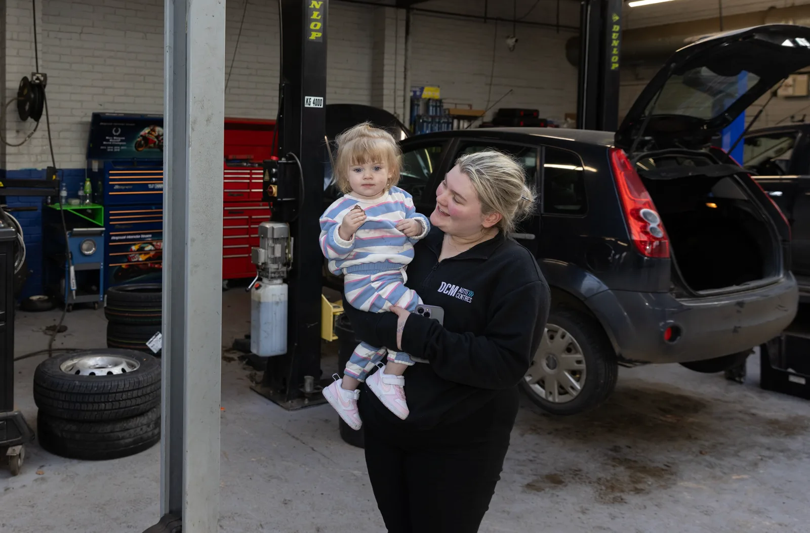 A parent holding a baby in the DCM Autocentres Shaftesbury workshop